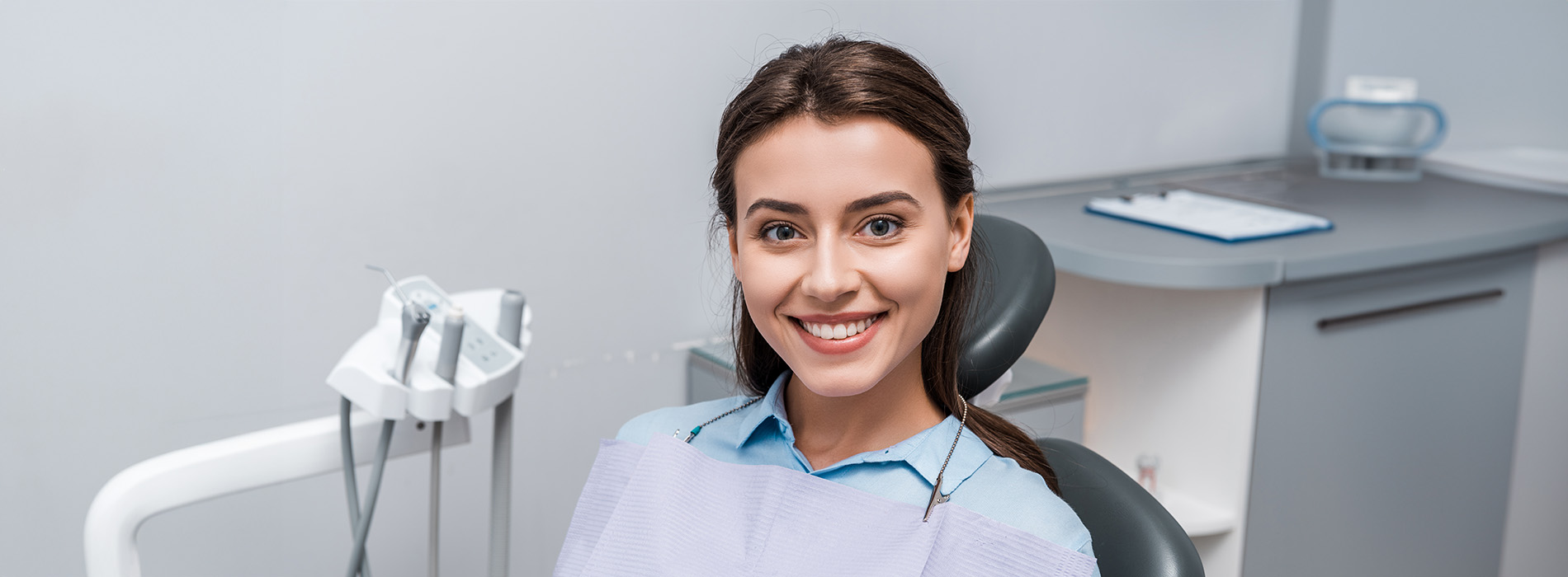 A person is seated in a dental chair, receiving care from a dental professional who stands behind them.